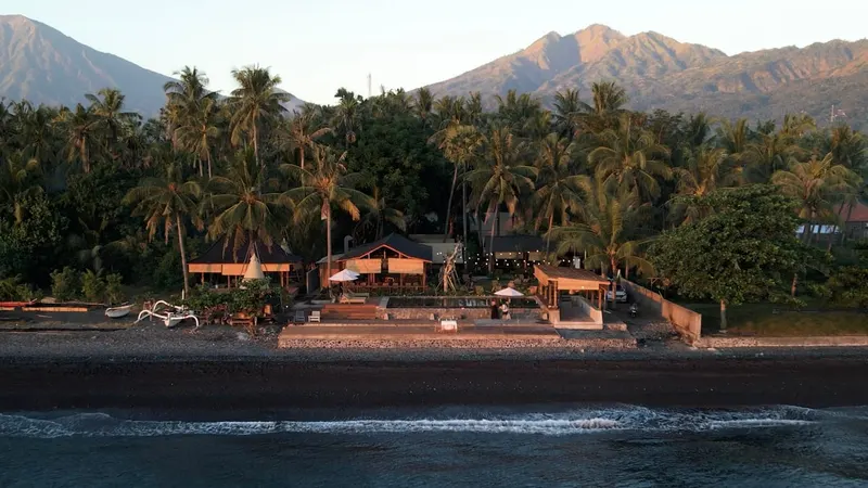 VELA Tianyar from the sea at dusk: Saga, the pool and the garden at the water, palms behind, Mount Agung above