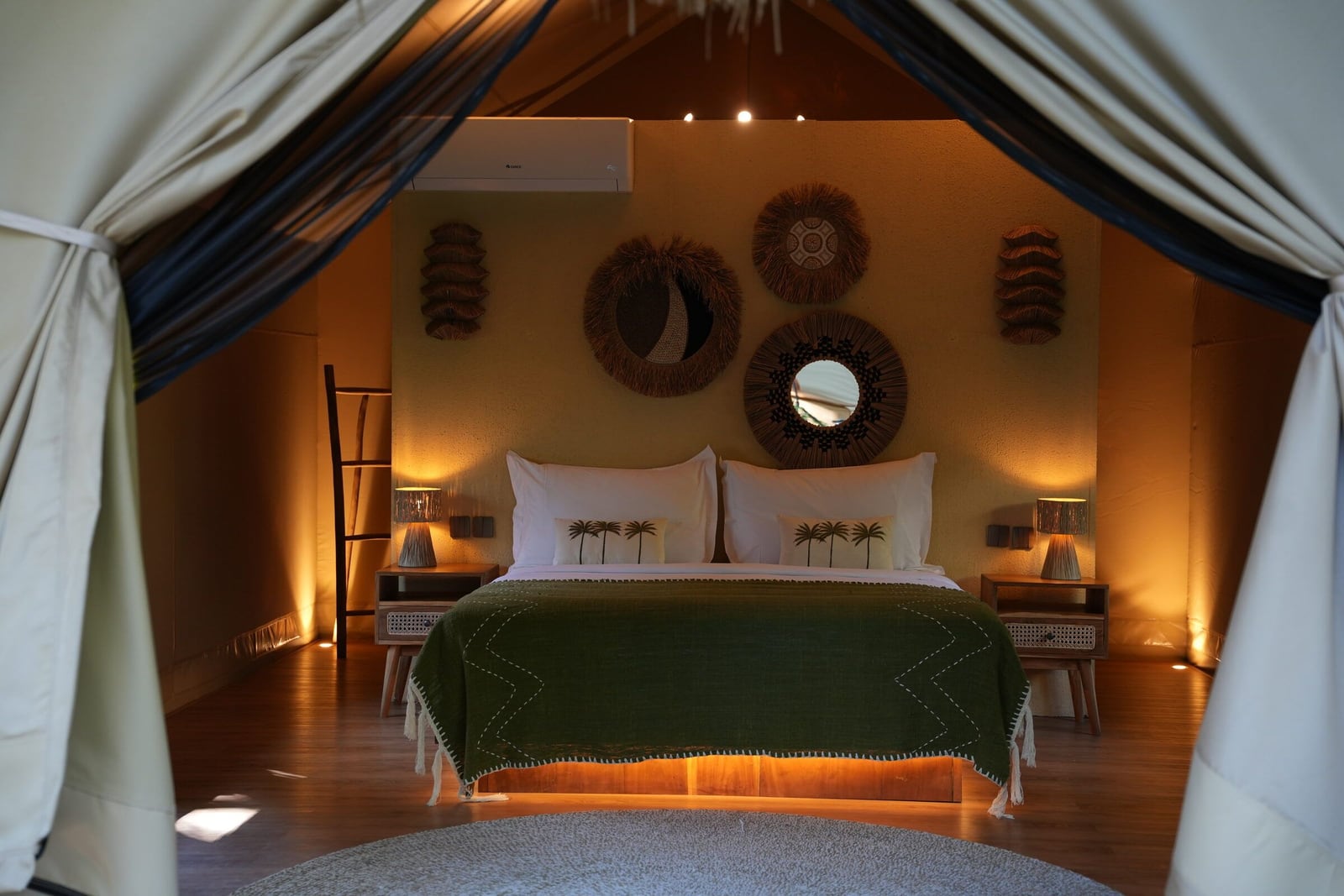 A lodge at dusk with the canvas doors tied back, the lamps on and the bed made