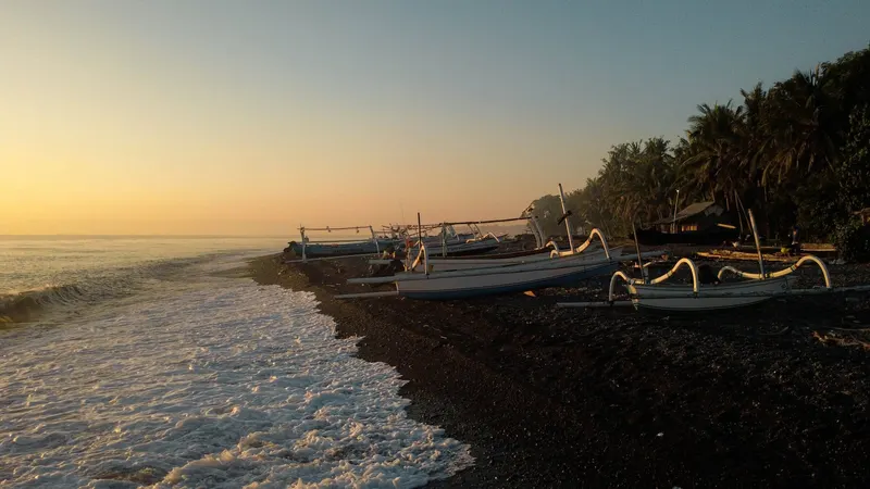 Jukungs pulled up on the pebble shore at Tianyar at sunrise, the sea gold behind them
