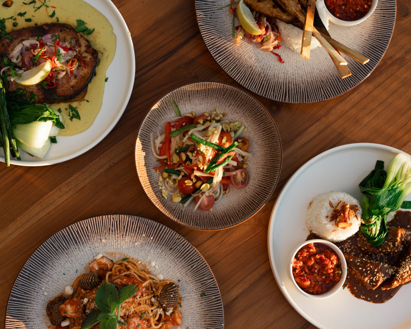 Five plates from the Saga kitchen on the teak table, seen from above, rice and sambal among them